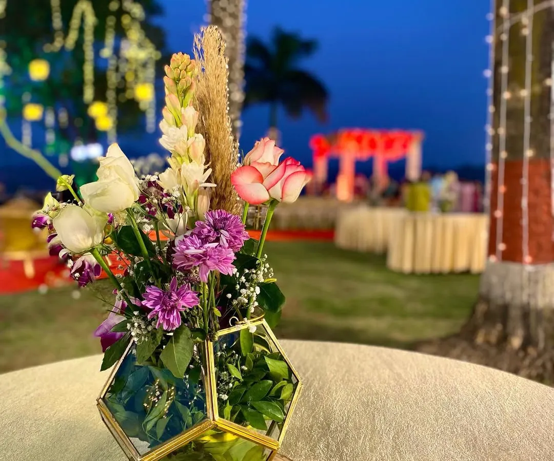 This is a modern centerpiece I made for an outdoor evening event. I used a hexagonal gold and glass terrarium vase and filled it with a mix of pink roses, purple carnations, white tuberoses, and a touch of dry pampas grass for a contemporary feel.
