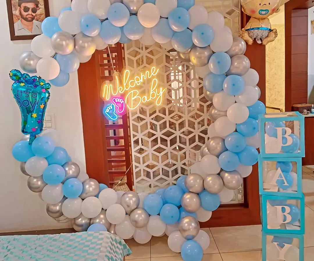 I create stunning welcome home decorations for baby boys, like this full balloon ring in shades of blue, white, and silver. The setup is completed with a "Welcome Baby" neon sign, "BABY" display boxes, and themed foil balloons.