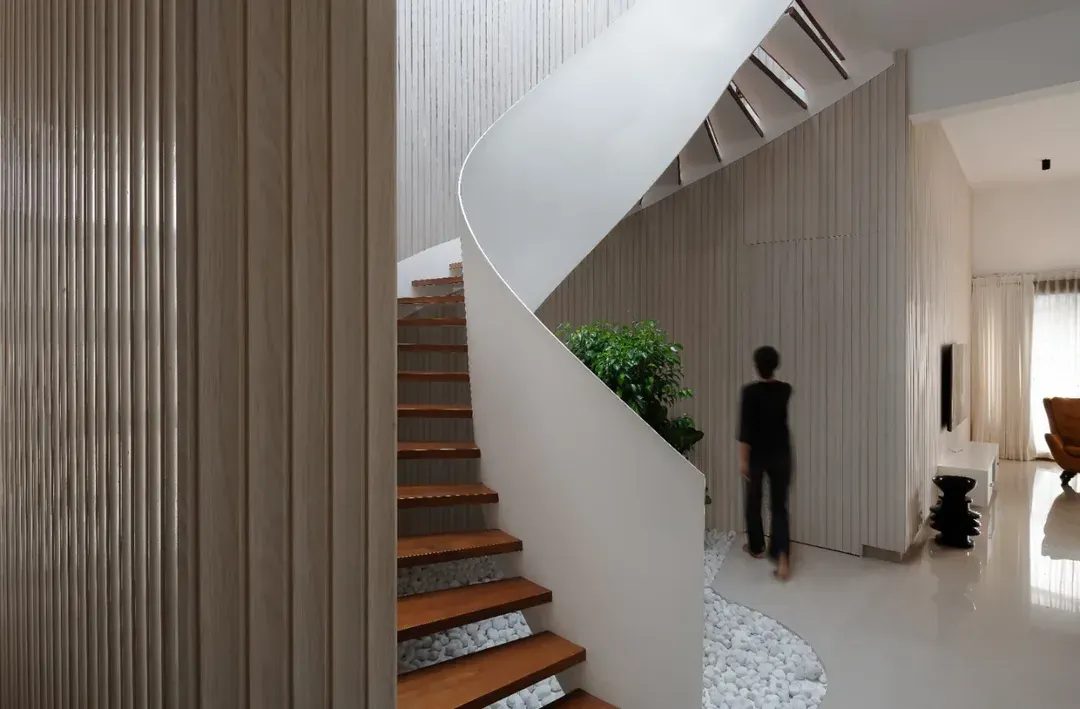 I believe staircases can be sculptural centerpieces. This helical staircase in a contemporary penthouse creates a striking visual impact with its dynamic, swirling form contrasted against the clean, linear aesthetic of the fluted wood wall.