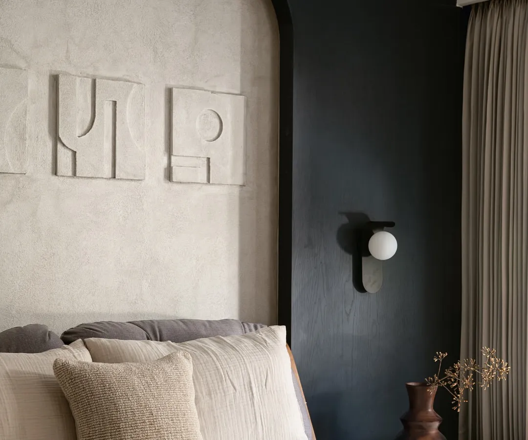 In this bedroom, I explored the power of a monochrome palette to create a space that is both youthful and sophisticated. The design is built on layers of texture, from the lime-washed wall behind the bed to the abstract art and soft linens. Every detail, including the modern wall sconce and custom headboard, was chosen to make the compact room feel intentional and full of character.