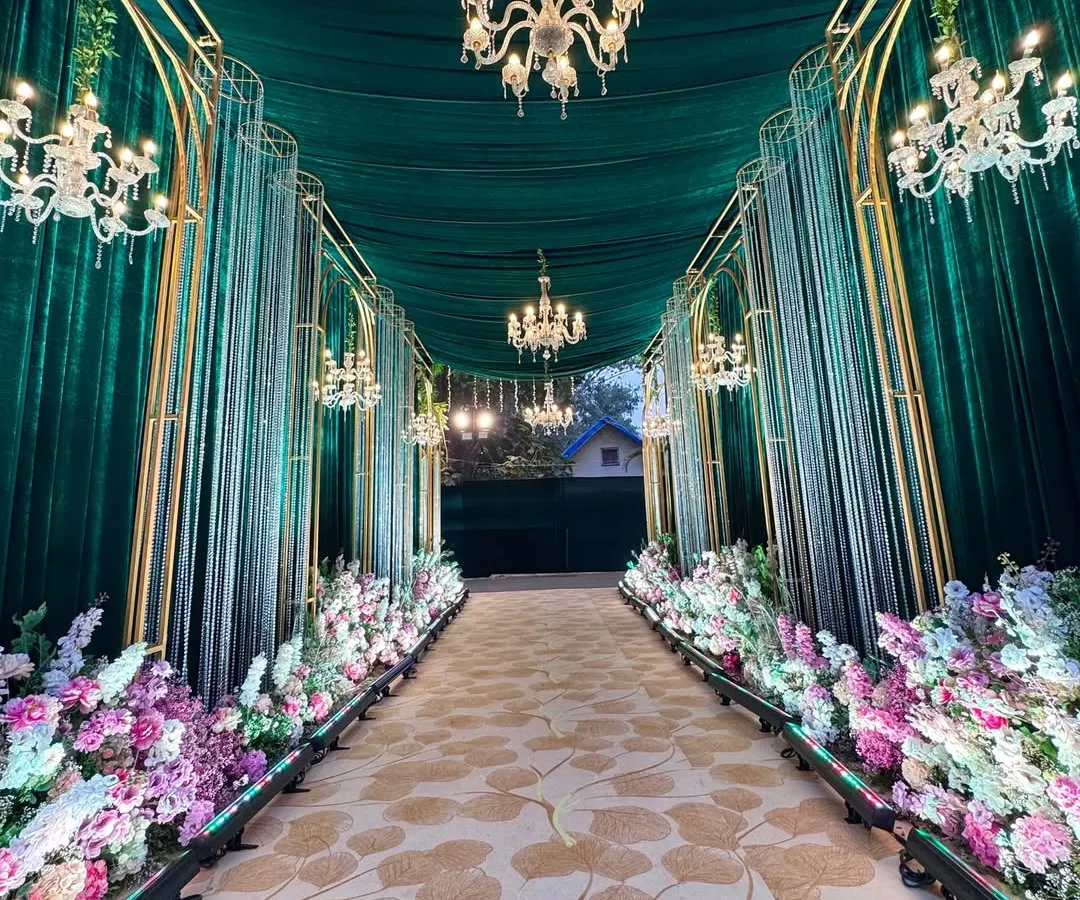 I design walkways that are an experience in themselves. Here, a path lined with lush florals and grand chandeliers guides guests through an emerald and gold archway, setting a tone of pure opulence.