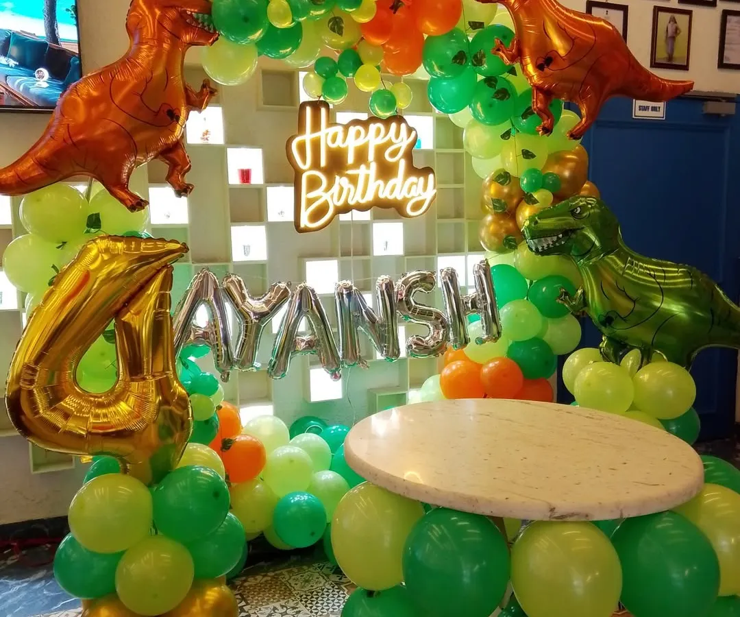 A dinosaur-themed birthday is always a hit with the kids. This setup includes a custom balloon arch with T-Rex foil balloons, a neon "Happy Birthday" sign, and a matching balloon-wrapped table for the cake.