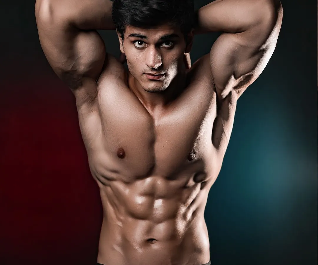 A modern athletic portrait using dual-tone red and blue lighting to add mood and dimension. The focus is on sharp abdominal definition and a confident, direct-to-camera pose for a high-impact fitness portfolio shot.