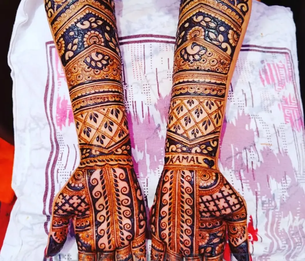 A beautiful example of full-arm bridal mehndi with heavy, intricate work. The design uses a mix of traditional jaal patterns and bold floral motifs to create a rich and dense look, perfect for a royal wedding theme.