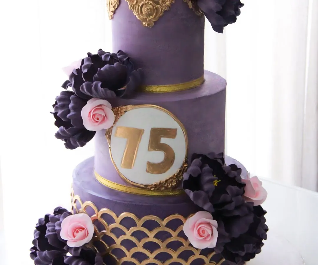 Celebrating 75 glorious years with a cake that’s fit for royalty. This three-tiered masterpiece features a regal purple ganache finish, intricate gold stenciling, and a cascade of handmade sugar peonies and roses. The top two tiers were a delicate pistachio rose, with a rich chocolate cake for the base.