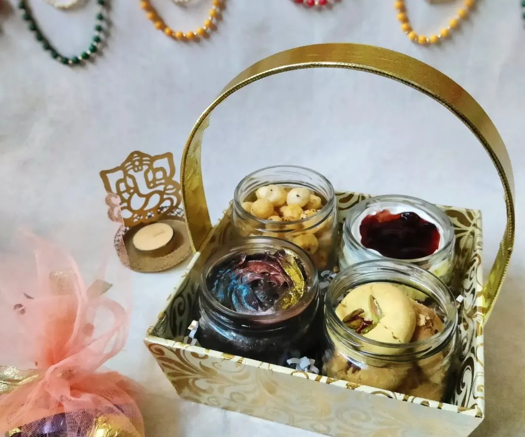 My Diwali hamper is a basket full of joy, combining sweet and savory treats. It includes two of my homemade cake jars, a jar of crunchy peri peri makhana, traditional pistachio nankhatai, and a little pouch of assorted chocolates.