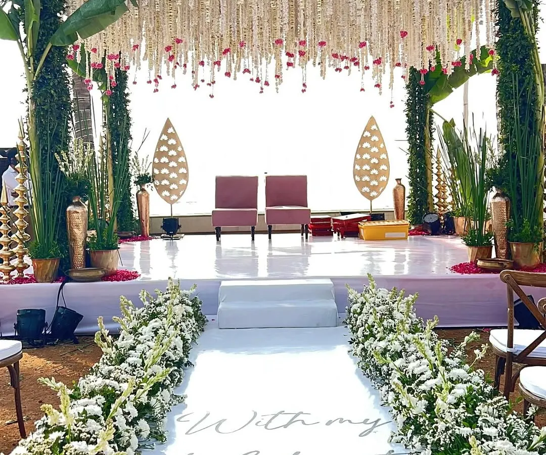 We designed this beautiful beach wedding aisle with a custom message that reads 'With my whole heart, for my whole life'. The walkway leads to a traditional stage framed by banana leaves and hanging tuberose garlands, blending coastal charm with classic elegance.