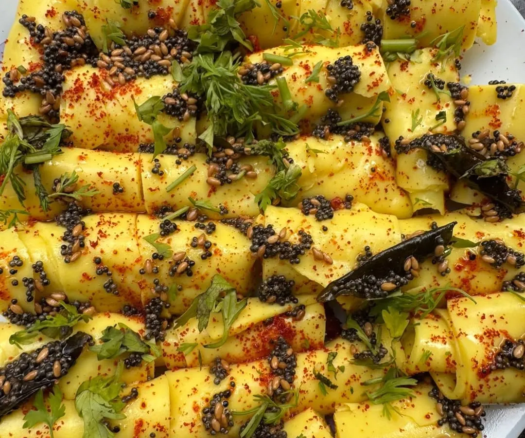 Our Khandvi is a true labour of love, made from scratch using a traditional recipe. These soft, delicate rolls are tempered with mustard seeds and garnished with fresh coriander, making them a perfect Gujarati snack for any occasion.