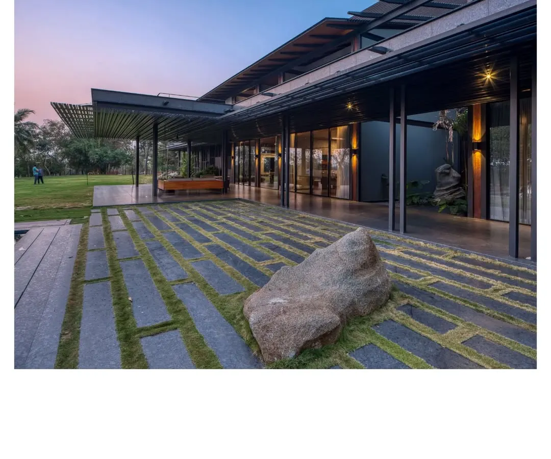 The Lakeshore house at dusk, a filter for breezes and views on Lake Osman Sagar. Here, a prefabricated steel skeleton and walls of rammed earth from the site itself come together, creating a home that almost disappears into the treeline.
