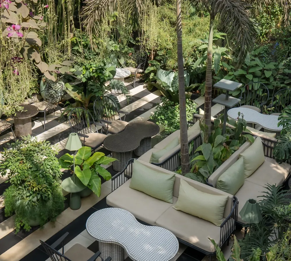 An overhead view reveals the spatial story of the garden court, a series of interconnected seating areas nestled within the greenery. The design encourages slow, meandering experiences, with custom furniture and varied layouts offering different perspectives of the lush, biophilic interior.