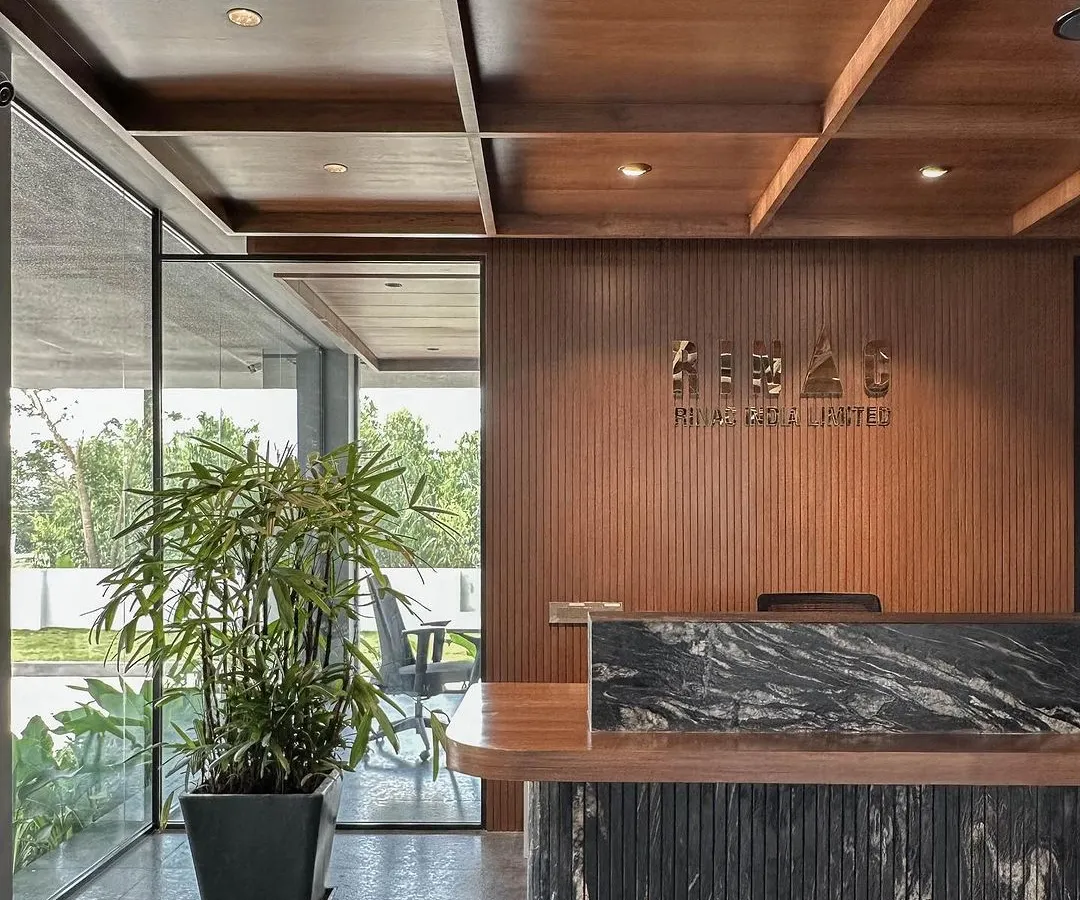 The reception area at RINAC Headquarters, designed to make a strong first impression. This space features a custom-designed desk with a fluted base and a dramatic black granite top, set against a backdrop of vertically grooved wood paneling and our signature coffered wood ceiling.