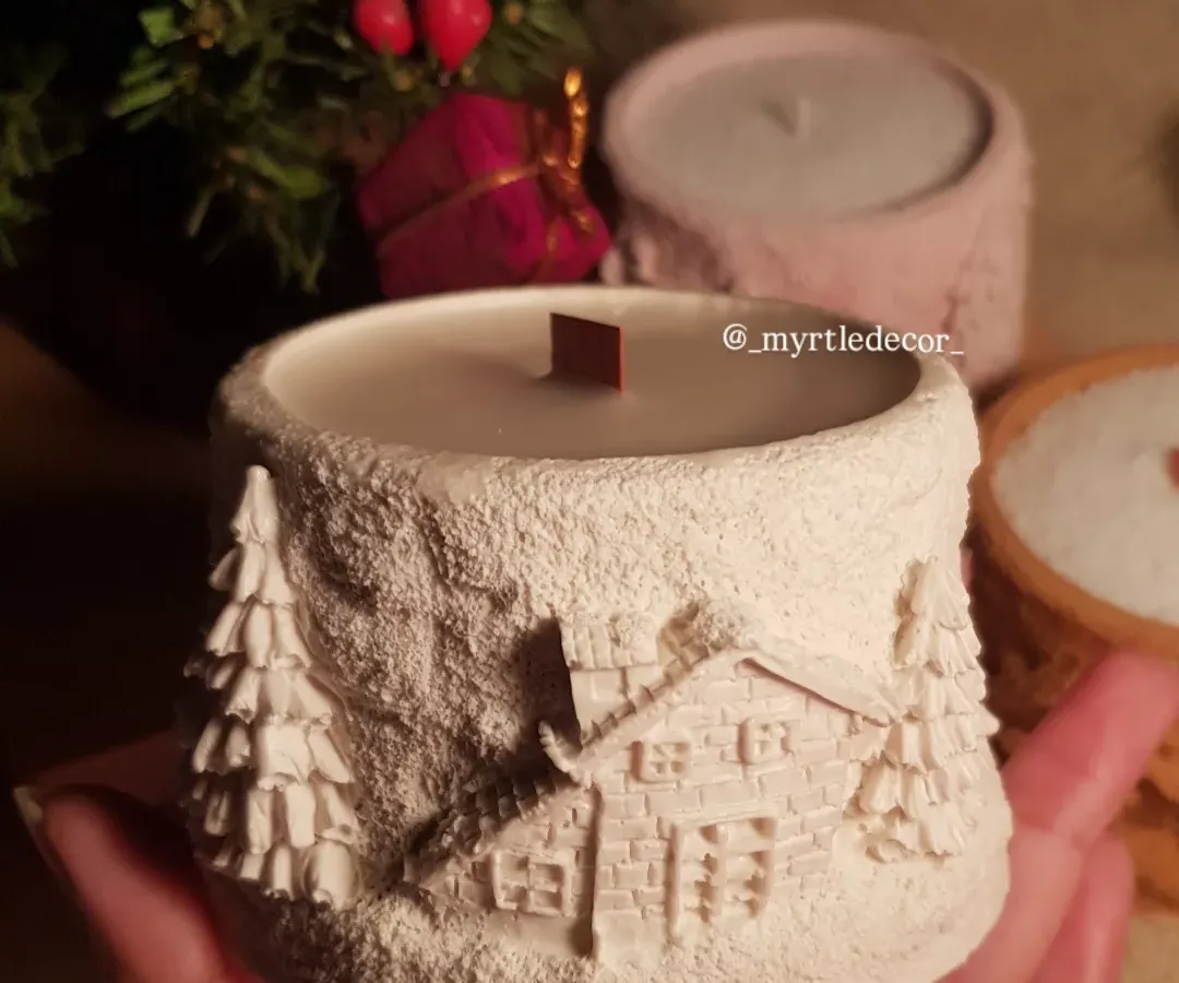 A closer look at our 'Winter Lights' jar candle, held in hand to show its comforting size and intricate, snowy cabin details. We pour these 100% soy wax candles ourselves, making them a perfect piece of warmth for any cozy corner or as a thoughtful Christmas gift.