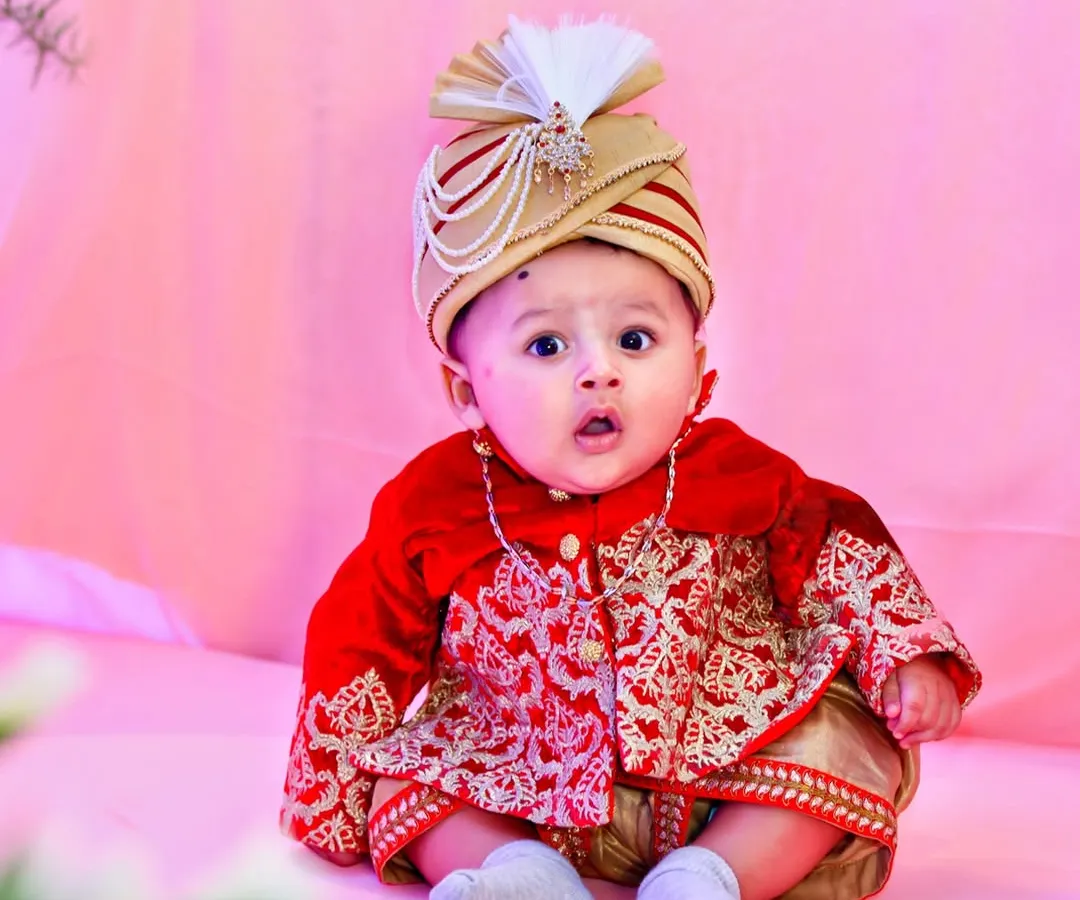 A vibrant, full-color portrait of a baby boy dressed in a traditional red and gold sherwani and turban. This shot highlights our ability to capture sharp, expressive images in themed setups.