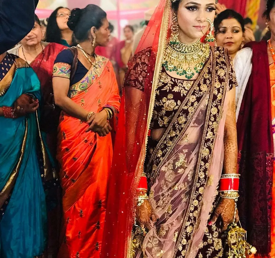 A beautiful bride on her wedding day, wearing a deep maroon velvet lehenga with intricate gold embroidery. This complete bridal look, including the double dupatta, is available for rent.