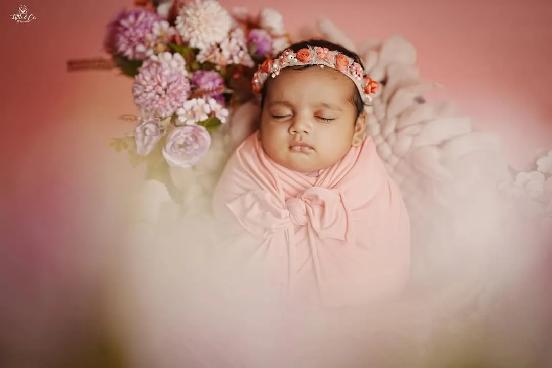 The pure innocence of a newborn is a fleeting moment we preserve forever. This studio shot uses soft lighting and a delicate floral theme to create a timeless portrait of a sleeping baby girl.