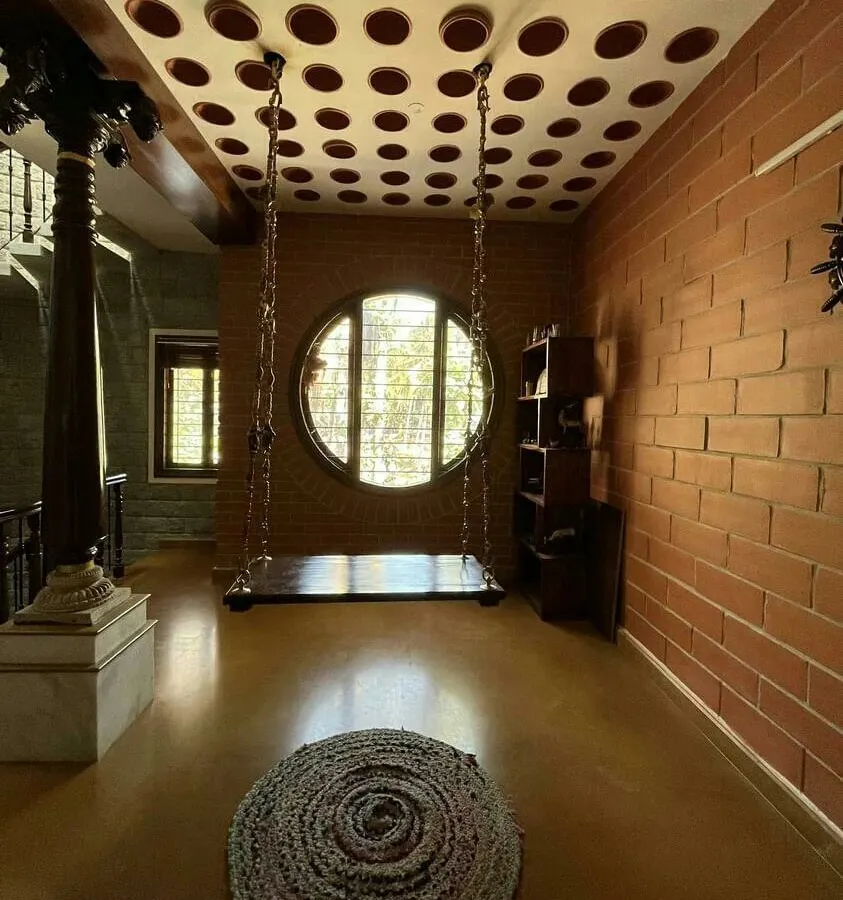 A quiet corner for reflection. This space combines a traditional indoor swing with a modern filler slab ceiling made of clay pots, reducing concrete usage while creating a unique visual texture. The large circular window frames the world outside, making nature a part of the home's interior life.