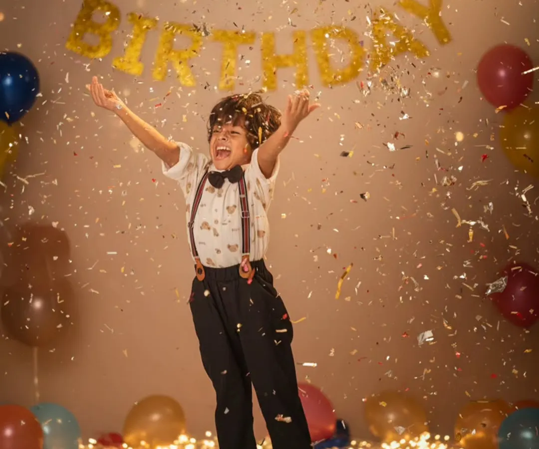 Capturing pure birthday joy as a young boy jumps mid-air, surrounded by falling golden confetti and a 'Happy Birthday' banner in the background.