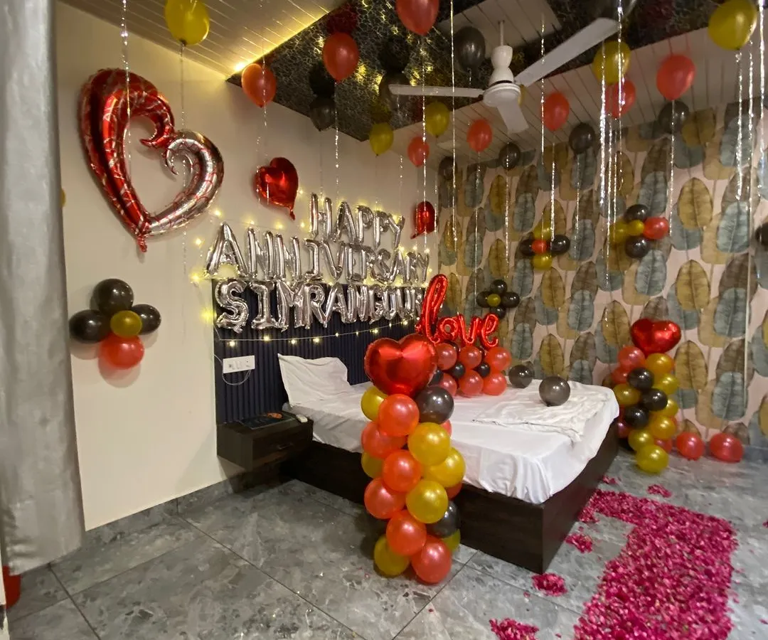 For this anniversary surprise, I created a full room transformation. The setup includes a custom foil balloon message with the couple's names, a romantic rose petal pathway leading to the bed, and a mix of red, yellow, and black balloons for a vibrant, celebratory feel.
