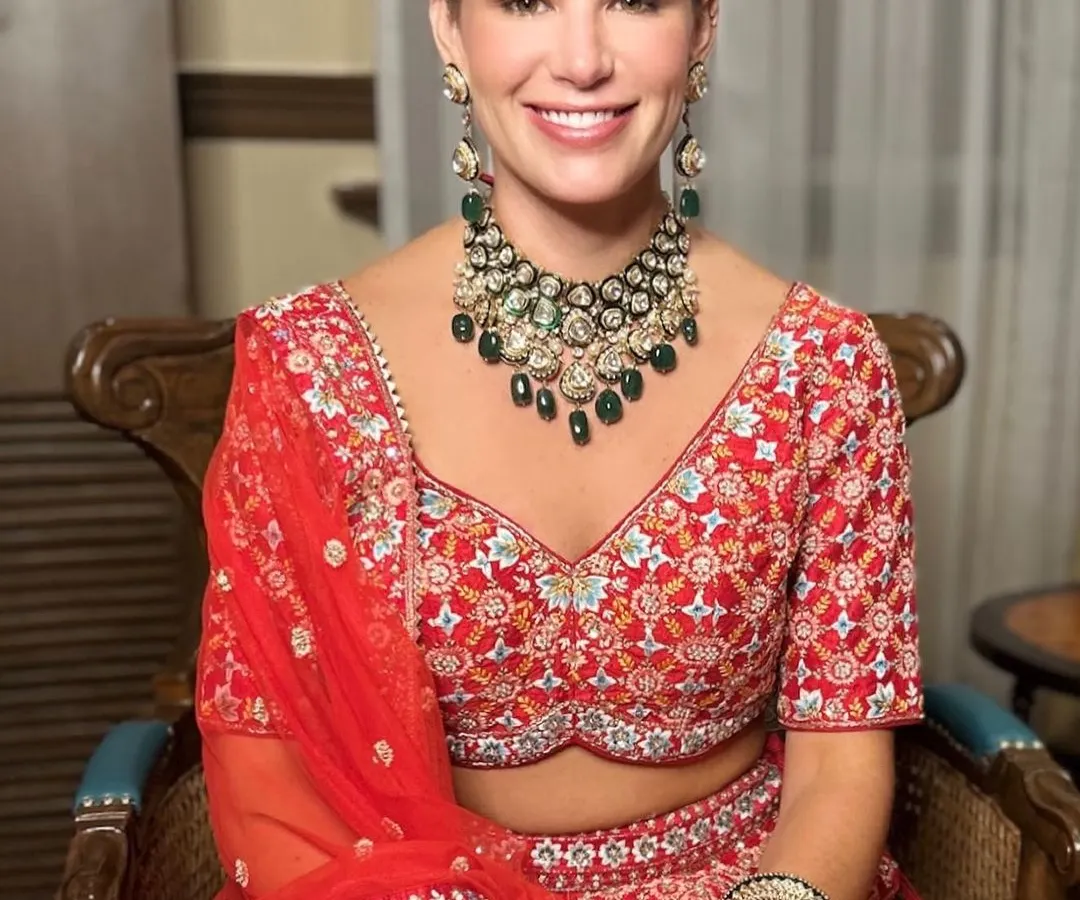 A beautiful smiling bride in her traditional red wedding lehenga. We focused on creating a luminous, long-lasting makeup base and defined eyes, paired with a classic bridal bun and maang tikka, for a truly timeless wedding ceremony look.