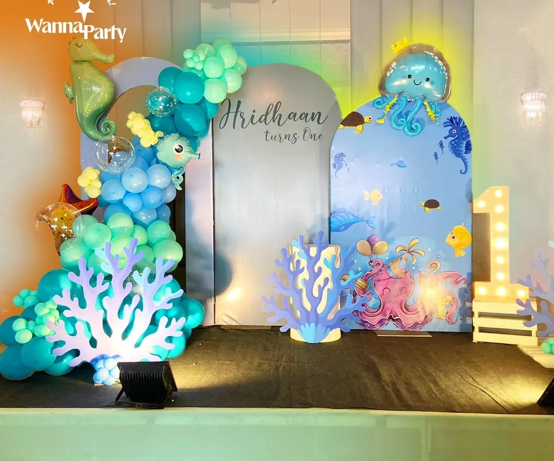 We dove deep to create this magical underwater world for a first birthday party. The setup features a custom backdrop with adorable sea creatures, an organic balloon garland in shades of ocean blue and teal, and charming cutouts of coral, a seahorse, and an octopus. The glowing "1" marquee light adds a special touch to this enchanting aquatic theme.