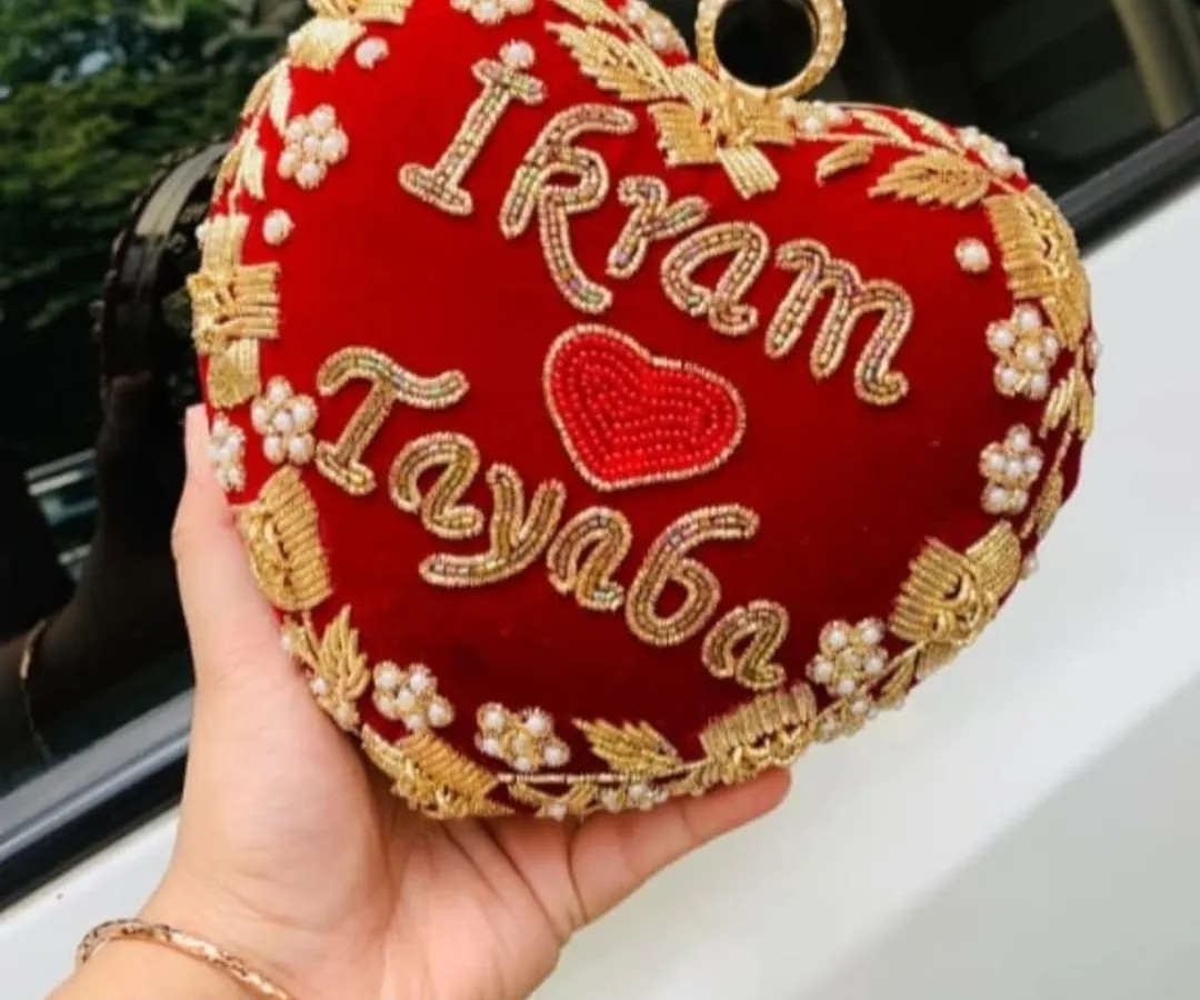 My heart-shaped bridal clutch, made from rich red velvet, is one of my favorite babies. I hand-embroider your names, like 'Ikram' and 'Tayaba' here, to make it a keepsake you'll treasure long after the wedding day. It's perfect for holding your phone and lipstick.