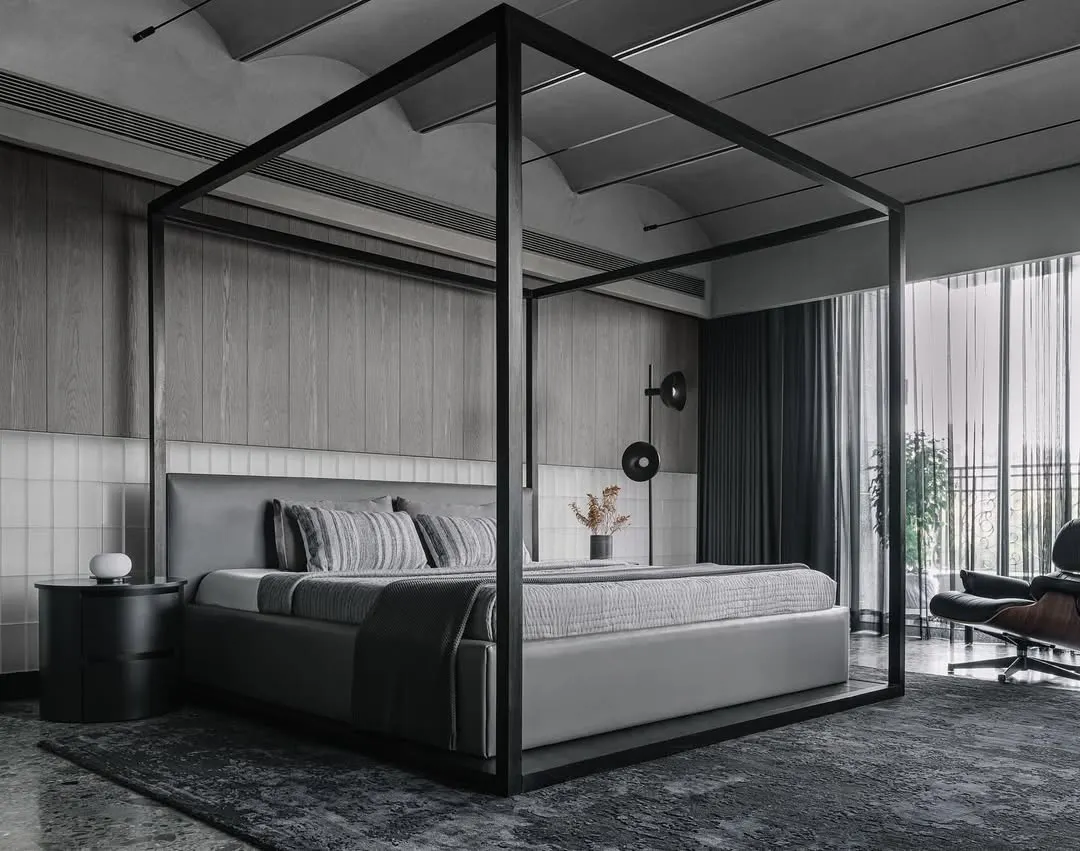 In this master bedroom from the Vaulted Haus, we used a four-poster bed to define the volume within the larger space. The headboard wall is a study in texture, combining frosted glass bricks with custom grey veneer strips. This layering of materials, along with the vaulted ceiling and tensioned rope lighting, creates a serene and sophisticated sanctuary.