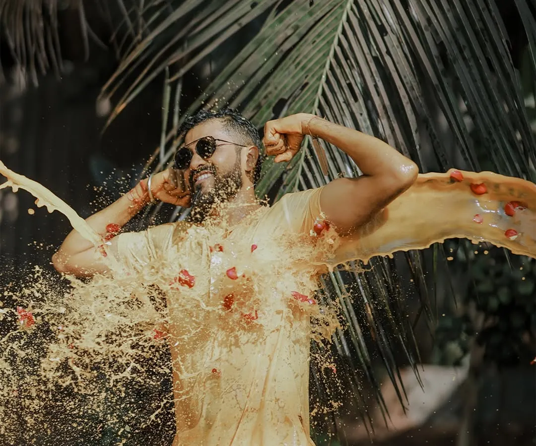 Capturing the pure, unadulterated fun of a Haldi ceremony. This high-energy shot freezes the moment the groom is joyfully drenched in turmeric paste and flower petals against a backdrop of lush palm leaves.
