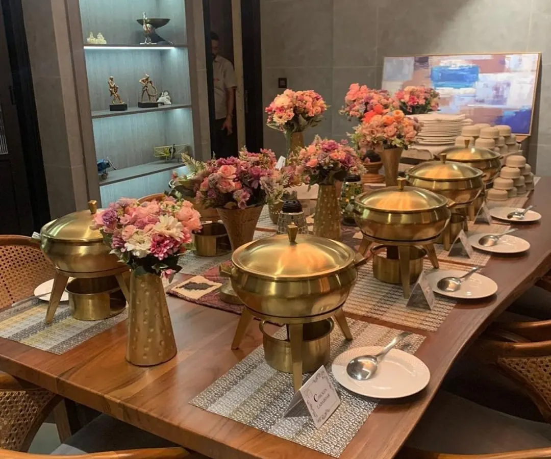 We transform any space into an elegant dining area. This is a glimpse of our classic buffet setup for an intimate corporate gathering, featuring our signature brass chafing dishes and coordinated floral arrangements.