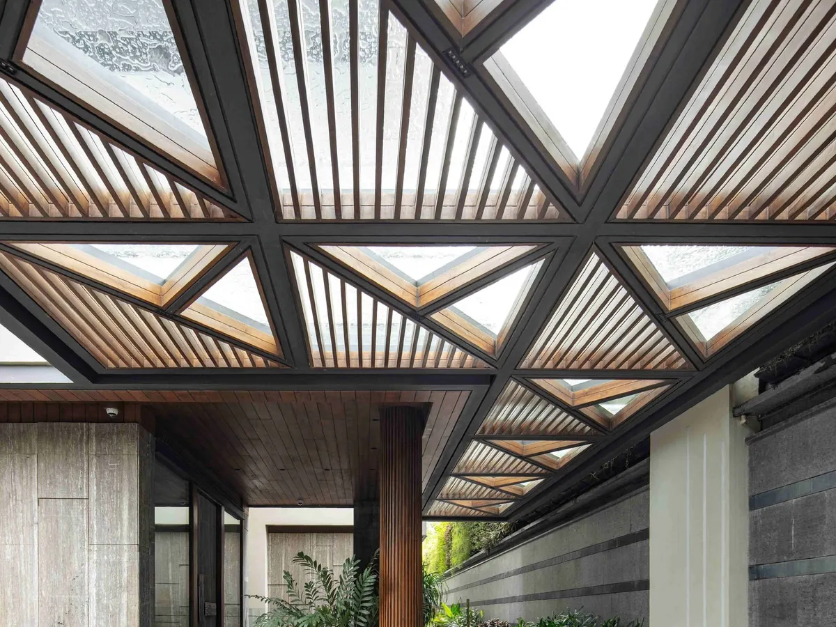 The entrance to the Bammi Residence is designed as a dramatic transition from the urban exterior to a serene interior. The geometric, slatted canopy filters natural light, creating dynamic patterns of light and shadow on the steps and water body below. This architectural feature sets a tone of thoughtful design and a deep connection to natural elements, which is a hallmark of our work.