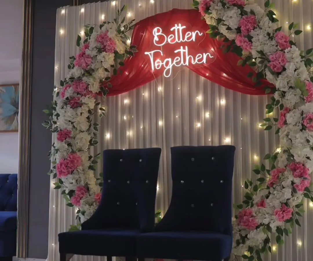 For a modern and romantic ring ceremony, we design backdrops like this one. It features a floral ring, soft drapes with fairy lights, and a custom neon sign like 'Better Together' to make your engagement stage truly personal.