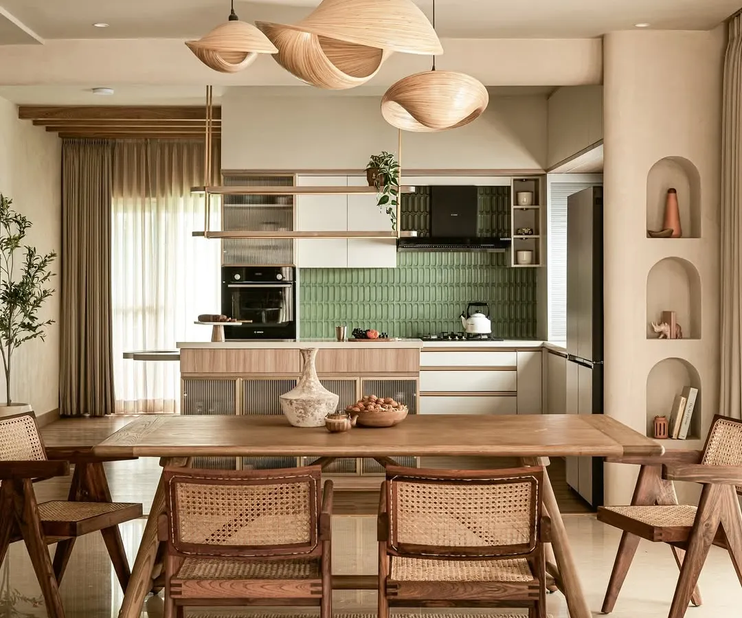 I design open-concept spaces where life flows seamlessly from one moment to the next. This view connects the dining area to the kitchen, unified by sculptural wooden pendant lights, natural materials like cane and teak, and architectural details like the recessed ceiling, demonstrating a complete and cohesive home vision.