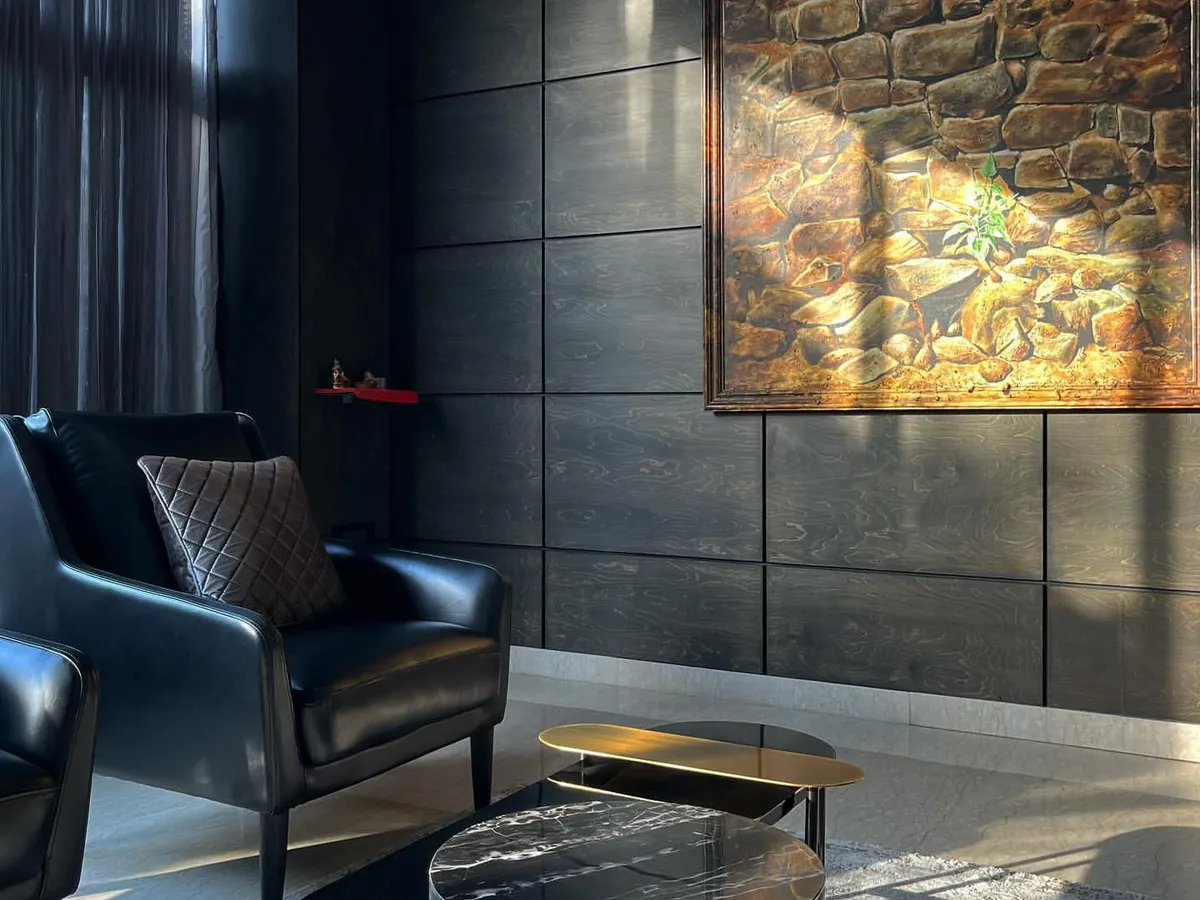 A quiet corner in an office we designed, demonstrating the power of chiaroscuro. We used a palette of dark, textured panels and leather, allowing natural light to carve out the space and highlight the artwork, creating a sophisticated and focused atmosphere.