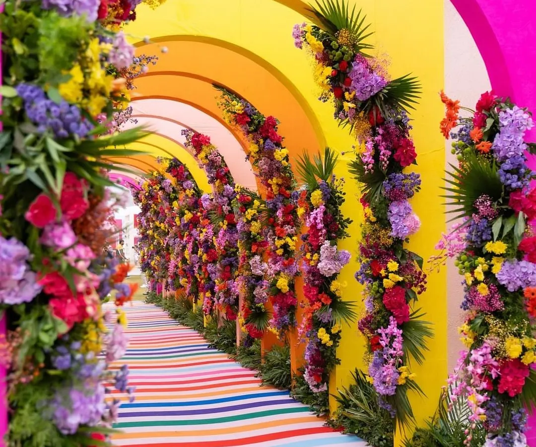 A spectacular rainbow tunnel entrance for a vibrant daytime event, using colorful floral arrangements on repeating arches to create an immersive and joyful welcome for guests.