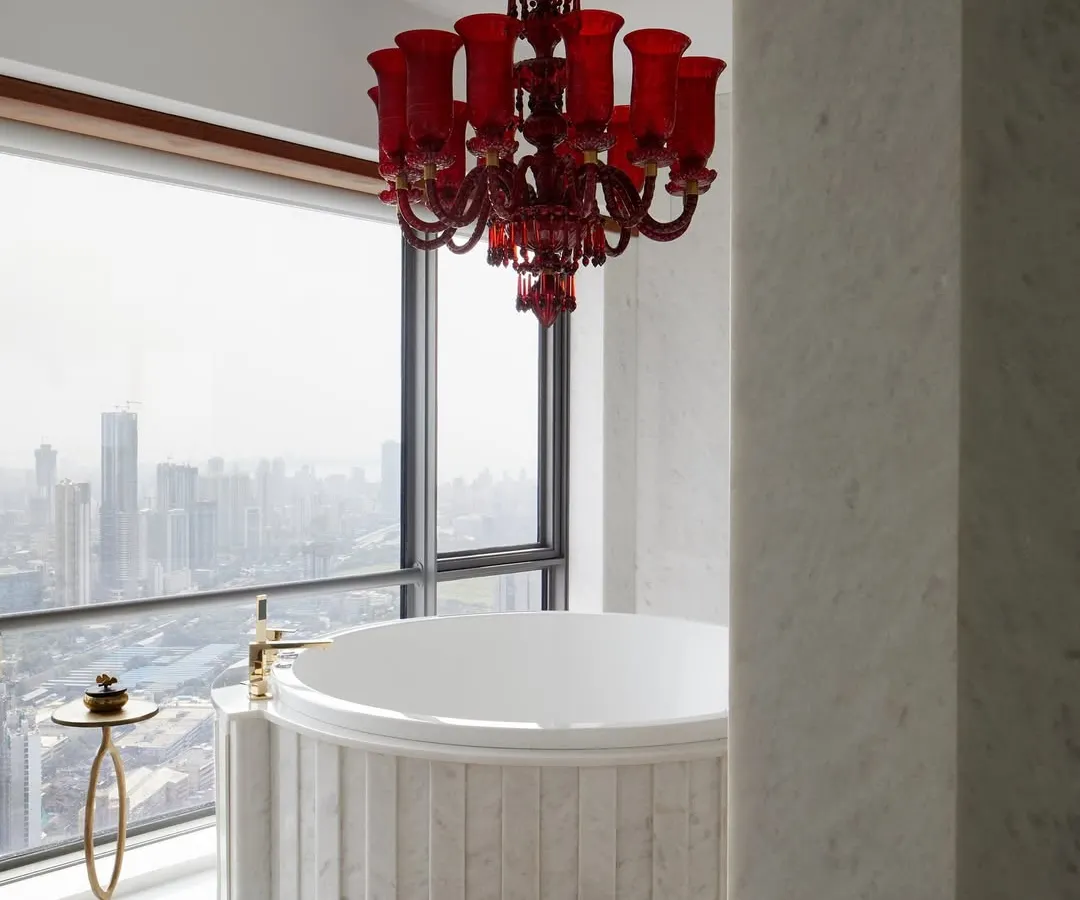 In this master bathroom high above the Mumbai skyline, luxury meets drama. A vintage red Murano glass chandelier hangs over a custom marble spa bath, creating a romantic and intensely personal retreat with an unparalleled view of the city.