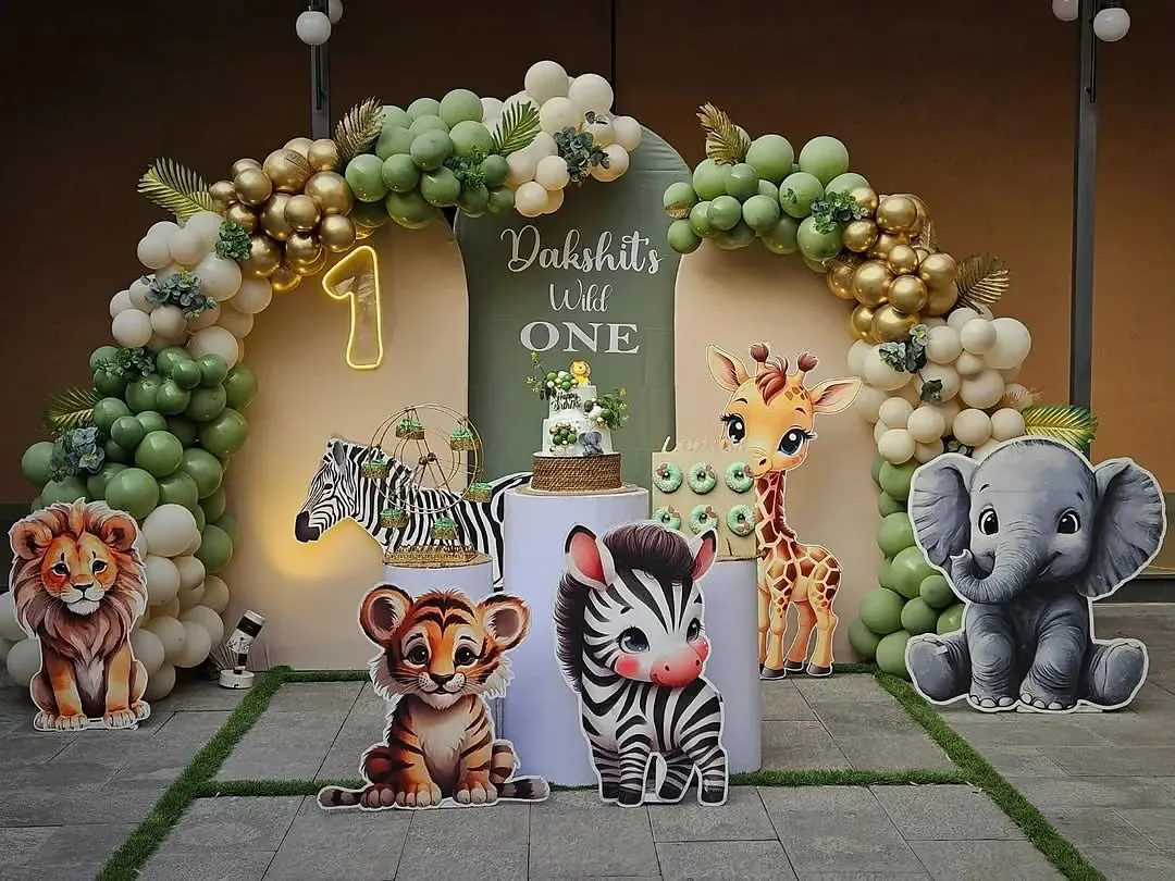 For little Dakshit's first birthday, we created a "Wild One" jungle safari theme. This adorable photo corner features cute animal cutouts, a lush balloon arch in sage green and gold, and a custom cake, setting the stage for a fun and memorable celebration.