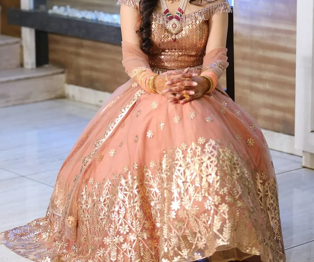 A full view of our peach off-shoulder gown, showcasing its impressive flare and intricate gold leatherwork. This modern rental piece is ideal for sangeet nights, receptions, or for a sister of the bride or groom.