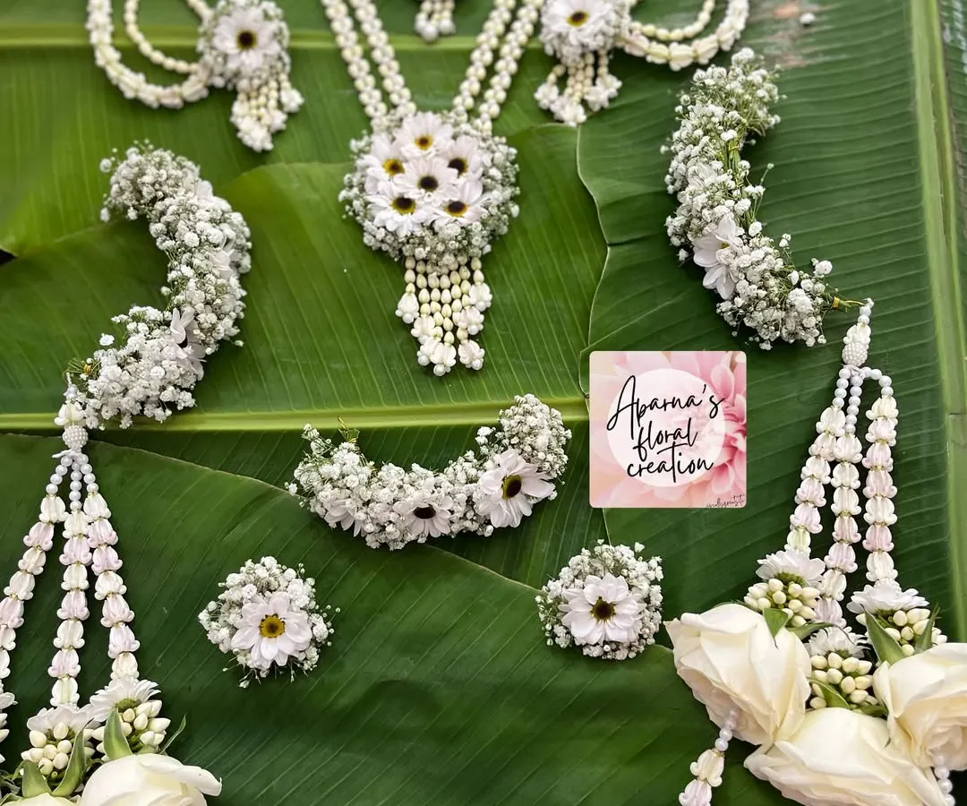 This is a full bridal Haldi jewellery set, handcrafted with white flowers, baby's breath, and pearls. The complete collection includes a necklace, earrings, maang tikka, bajuband (armlets), hath phool (hand harnesses), and matching floral kaliree.
