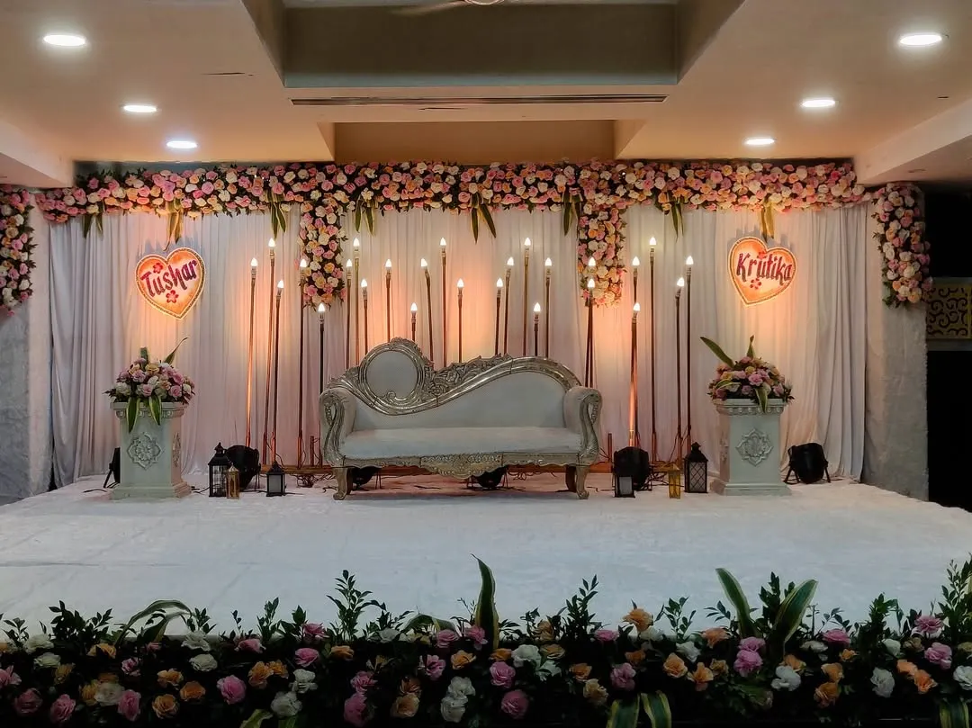 I designed this elegant engagement stage for an indoor hall. The setup features a classic white chaise lounge, a backdrop of warm candle-style lights, and a full floral border, creating a romantic and sophisticated look.