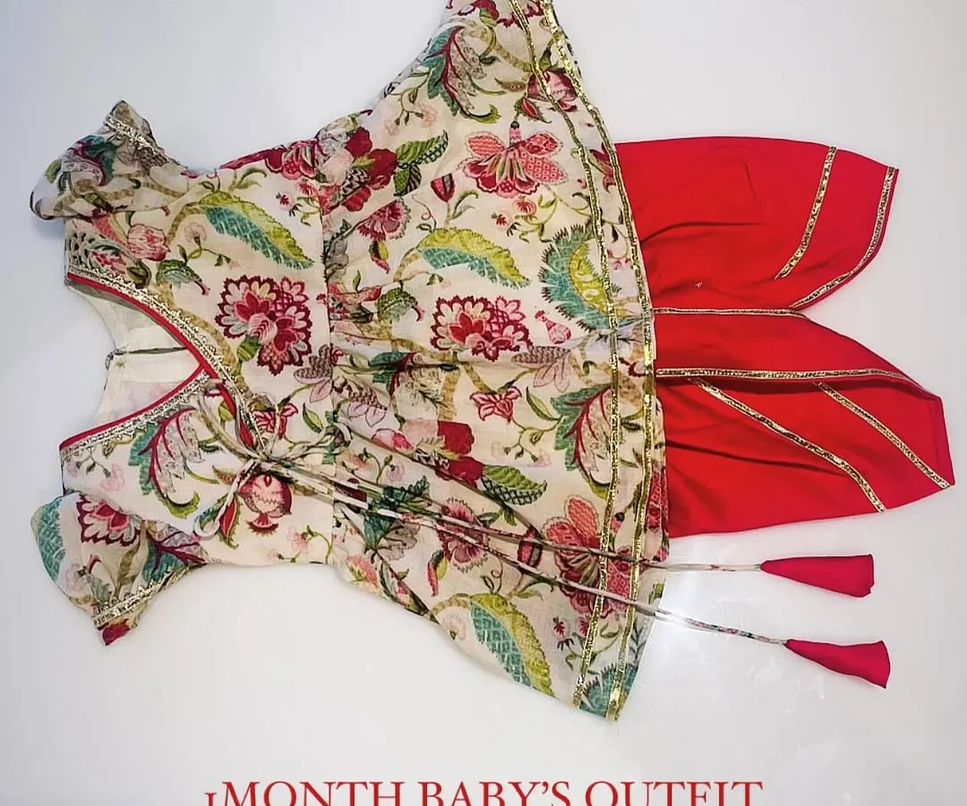 This complete festive set for a one-month-old baby includes a traditional floral print Angrakha top with tassel ties, paired with comfortable red dhoti pants finished with gota patti borders. It's designed for both style and comfort during family celebrations.