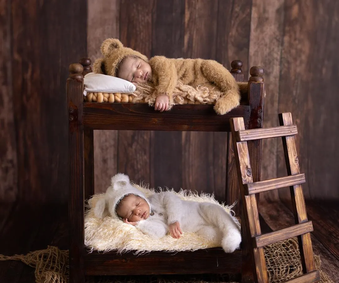 An artistic and heartwarming newborn portrait of twins, each sleeping peacefully in their own level of a miniature wooden bunk bed. This shot highlights our creative and safe approach to capturing your baby's first precious moments.