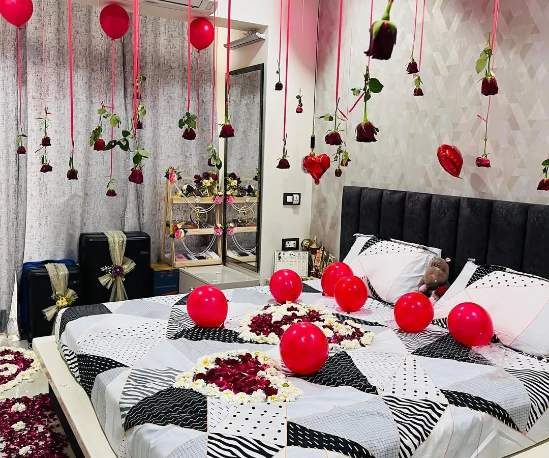 I focus on the small details that make a big difference. Here you can see the intricate heart-shaped art I create on the bed using red and white rose petals, surrounded by more balloons. Real red roses and heart ornaments hang from the ceiling, adding a touch of elegance to the romantic setup.