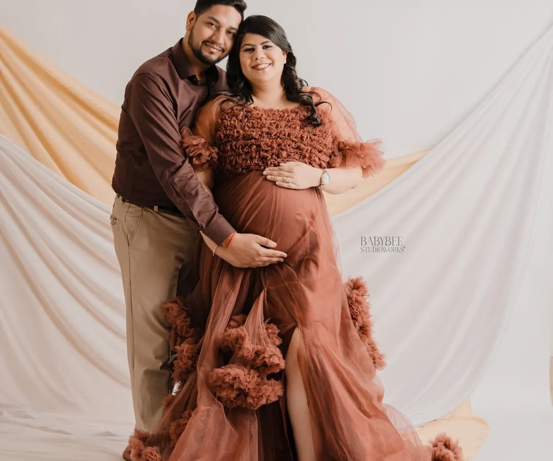 A glamorous maternity photoshoot featuring an expecting couple. The mother-to-be wears an elegant, flowing gown that highlights her baby bump, creating a truly special and celebratory portrait.