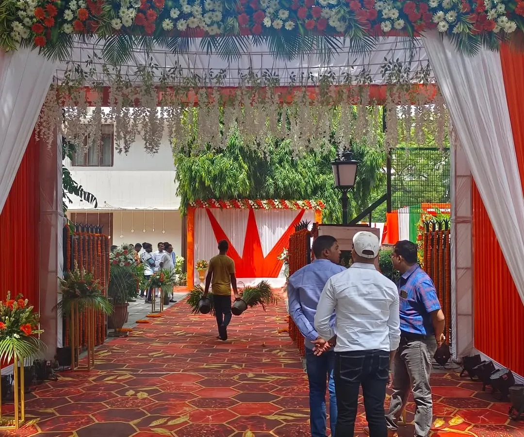 For a political leader's event, I created this entrance gate using a tricolor theme with saffron and white drapes and a dense floral border. The setup includes a clean, patterned carpet walkway and floral stands, making a professional first impression for arriving guests.