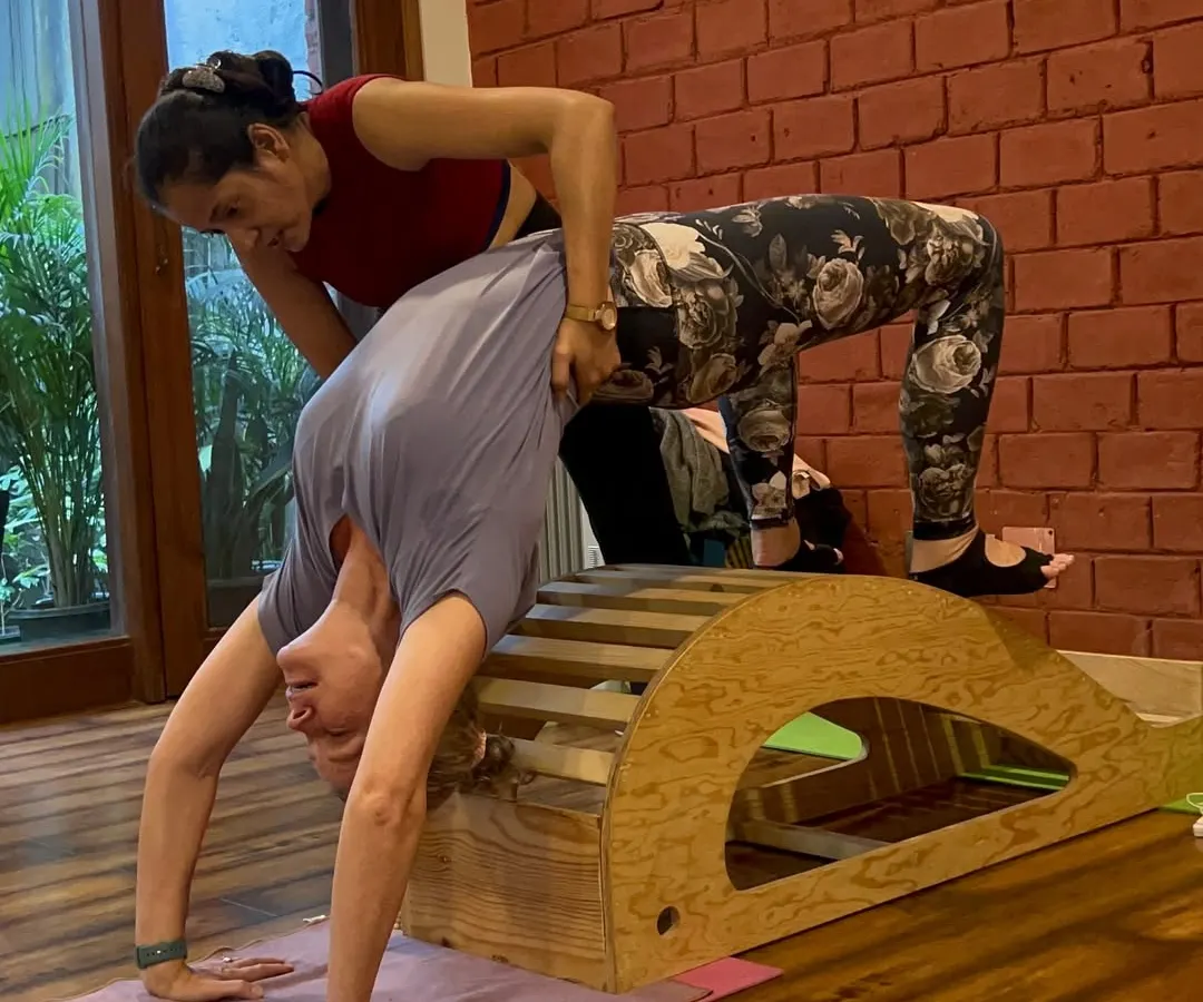 My approach to teaching is hands-on and personalized. Here, I am helping a student safely deepen her Chakrasana (Wheel Pose) using a spine corrector prop. This is how we build strength and flexibility with proper alignment, ensuring you learn the correct technique from day one.
