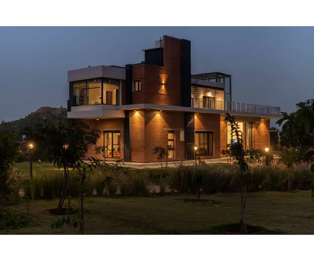 The Nandi Hills residence illuminated at dusk. We used strategic architectural lighting to highlight the building's form and warm brick texture, creating an inviting glow that integrates the home into its natural, grassy surroundings.