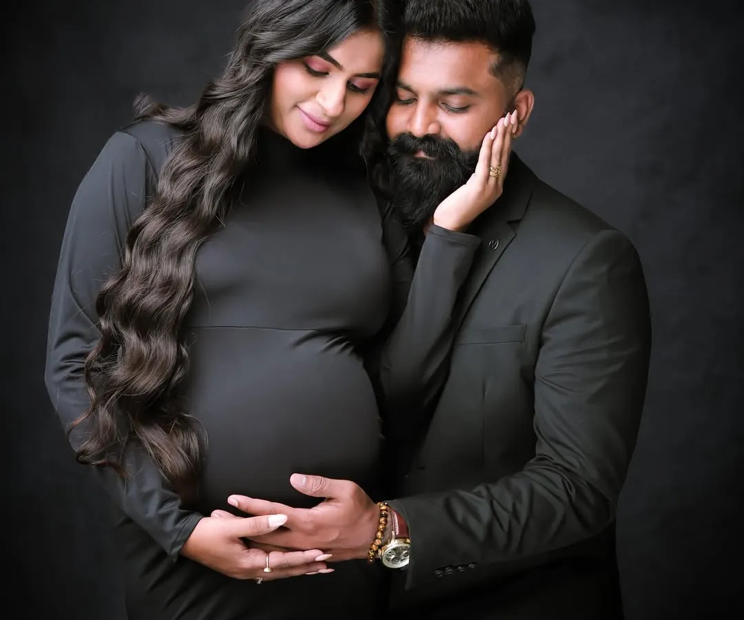 We capture the deep connection between partners with classic, intimate portraits like this one. This couple's portrait, set against a simple dark backdrop, emphasizes emotion and the shared excitement of expecting.