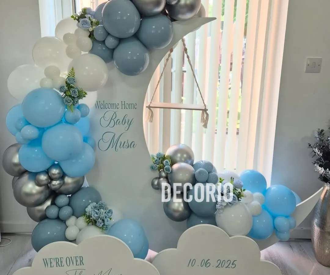 For a dreamy welcome home party, I created this "Over the Moon" setup. It features a custom-built moon prop with a tiny swing, surrounded by a cloud of blue, white, and silver balloons, making it a perfect welcome for a baby boy.