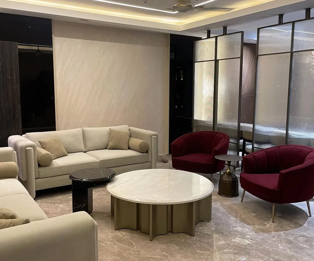 We designed this contemporary living room to feel luxurious and inviting. The centerpiece is a custom Italian stone coffee table, complemented by deep red accent chairs that add a vibrant pop of color. The large nine foot sofa, upholstered in soft suede velvet, offers ultimate comfort.