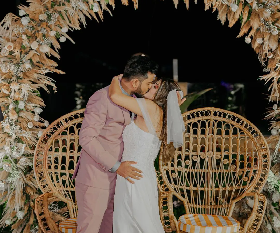 A passionate kiss seals the promise under a beautiful bohemian pampas grass arch at a Goa beach wedding. This frame captures the peak emotion and stunning decor of a modern coastal ceremony.
