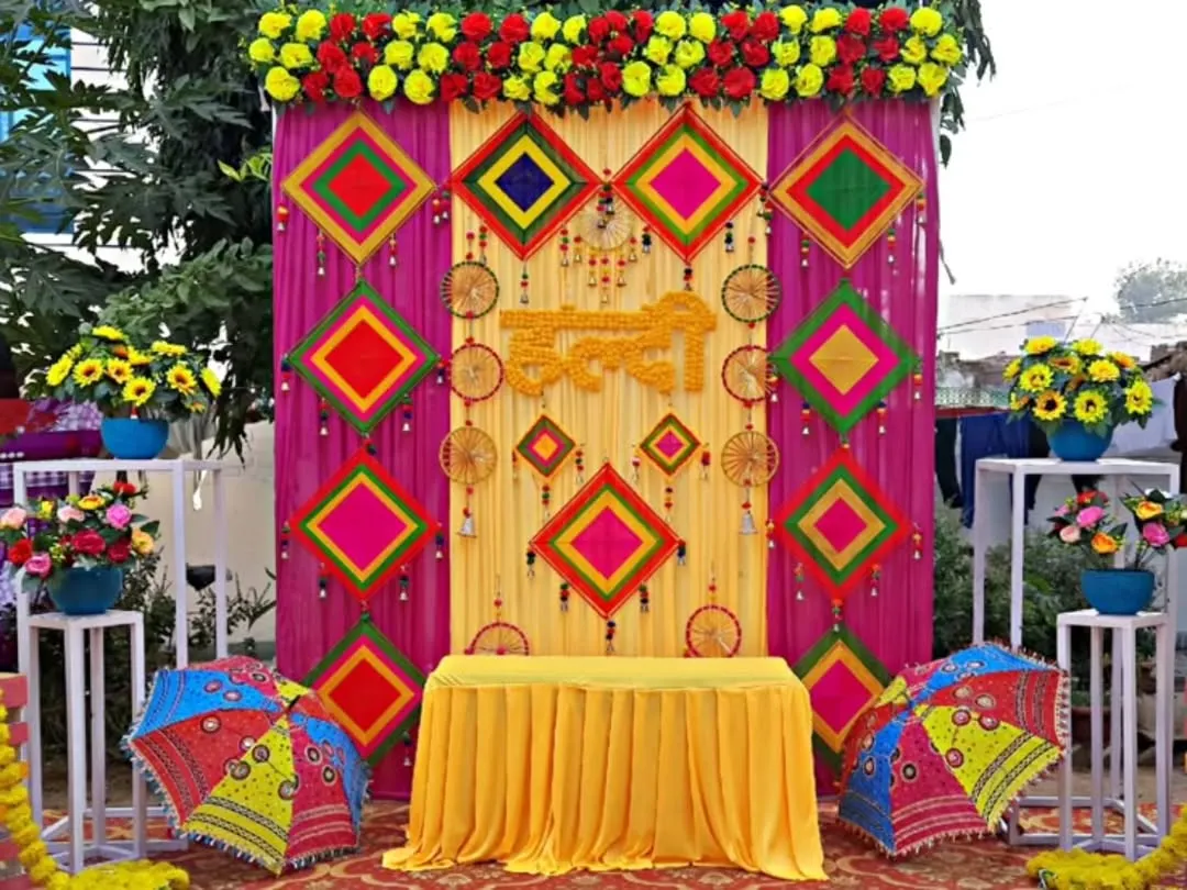 Here is a vibrant Haldi ceremony backdrop, bursting with color. I used traditional elements like Rajasthani umbrellas, colorful kite-shaped hangings, and a mix of real and artificial flowers to create a truly festive atmosphere for this outdoor event.